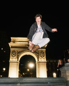 a man is jumping in the air on his skateboard near an arch at night