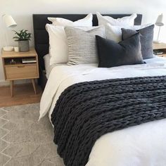 a bed with black and white pillows on top of it next to a night stand