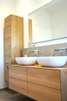 two white bowls sit on top of a wooden cabinet in front of a large mirror