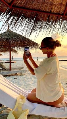 a woman sitting on the beach taking a photo with her cell phone