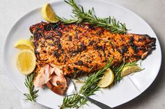 grilled fish with lemons and rosemary on a white plate, ready to be eaten