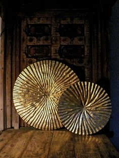 two large gold plates sitting on top of a wooden table next to a wall mounted clock