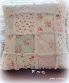 a white pillow with pink flowers and ruffles on the front is sitting on a table