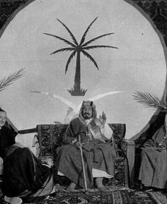 an old black and white photo of two men sitting in front of a palm tree