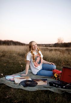 a young woman sitting on top of a blanket next to a record player in a field