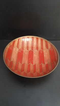 a red and gold plate sitting on top of a black table next to a wall