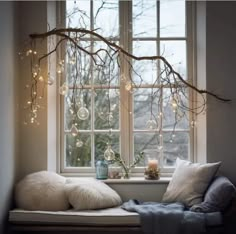 a window seat with pillows and lights hanging from it's windowsill in front of a tree branch