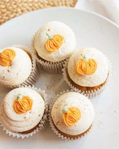 six cupcakes with white frosting and orange icing on top are sitting on a plate