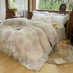 a bed with pink flowers and ruffled bedspread on it in front of a window