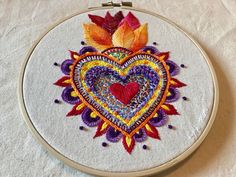 an embroidered heart on a white cloth with orange, red and yellow leaves in the center