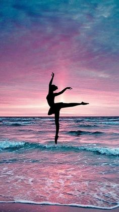 a person standing on the beach with their arms in the air while doing a dance pose