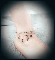 a person with a ankle tattoo on their left foot is wearing a beaded chain