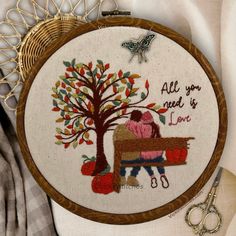 a cross stitch pattern with a couple sitting on a bench next to a tree and the words all you need is love