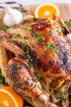 a whole chicken on a cutting board with oranges and garlic