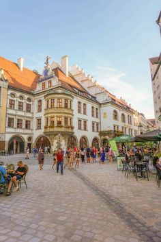 many people are sitting and walking around in the city square with tables, umbrellas and chairs