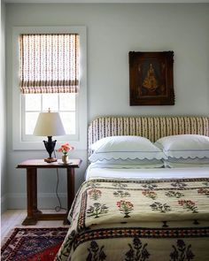 a bed sitting under a window next to a table with a lamp on top of it