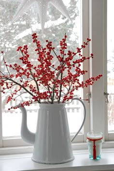 a white pitcher filled with red berries on top of a table next to a window