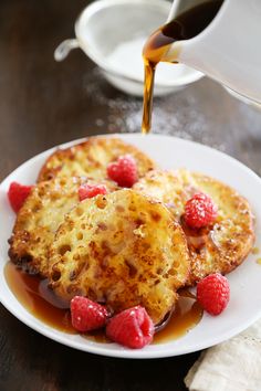 pancakes with raspberries and syrup on a white plate, being drizzled with maple syrup