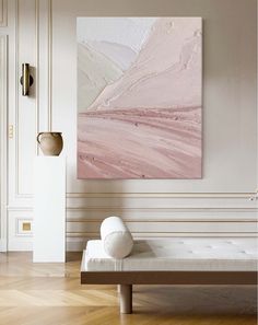 an abstract painting hangs on the wall next to a white bench in a room with wood flooring