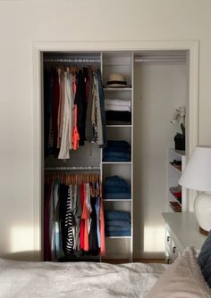 an open closet with clothes on hangers and folded shirts in it, next to a bed