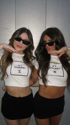 two beautiful young women standing next to each other in front of a white wall wearing black shorts