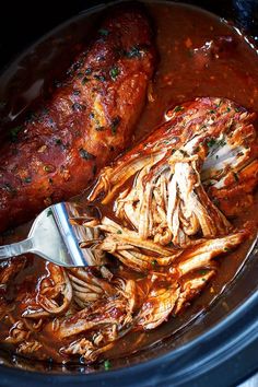 the meat is being cooked in the slow cooker with tongs and sauce on it