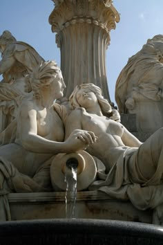 a fountain with statues surrounding it and water coming out of the top, in front of a blue sky