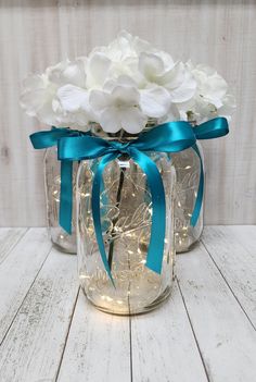 two mason jars filled with white flowers and blue ribbon