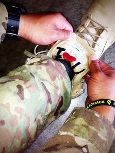 a person in camouflage is tying a shoelace to a sneaker that has a red heart on it