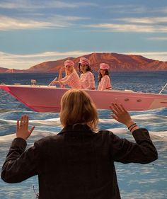 a group of women riding on top of a pink boat in the ocean with mountains in the background