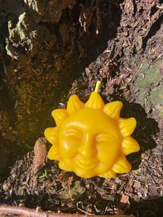 a yellow plastic sunflower sitting on the ground next to some dirt and mossy rocks