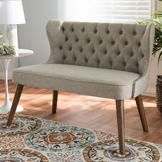 a beige chair sitting on top of a wooden floor next to a white vase filled with flowers