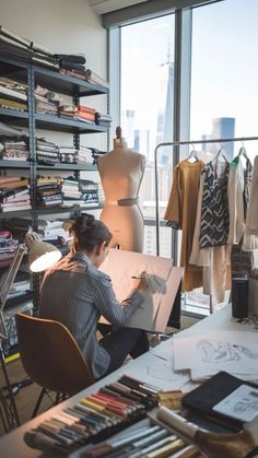 a woman sitting at a desk in front of a large window with clothes on it