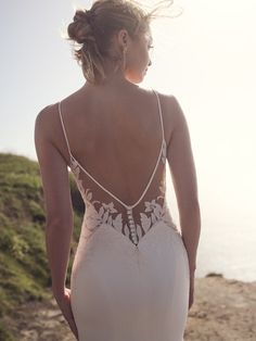 a woman in a white dress standing on the beach with her back to the camera