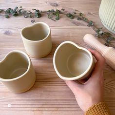 someone is holding three cups in their hand on the table next to some plant life