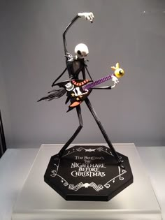 a skeleton playing a guitar on top of a black and white plaque in a glass case