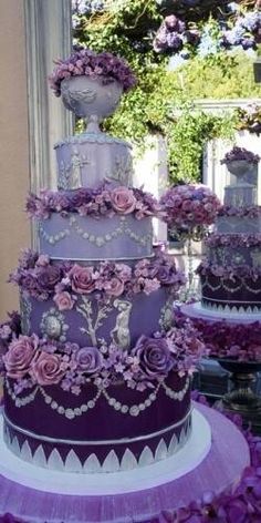 a purple wedding cake with lots of flowers on the top and bottom tier, sitting in front of a window