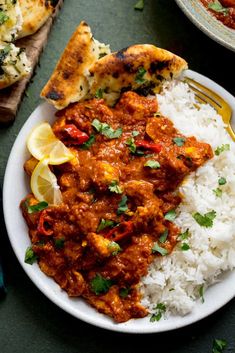 a white plate topped with rice and chicken curry next to two slices of flat bread