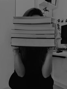 a woman sitting in front of a computer holding a stack of books over her head