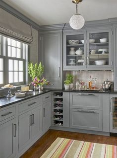 a large kitchen with gray cabinets and wooden floors is pictured in this image, there are many dishes on the counter