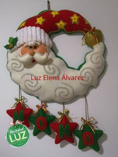 a santa clause ornament hanging from a wall with christmas decorations around it and the words luz elena alvarez written in spanish