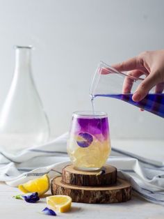 someone is pouring something into a glass with lemons and blueberries on the side