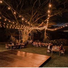 people sitting at tables under string lights in an outdoor setting with a wooden dance floor