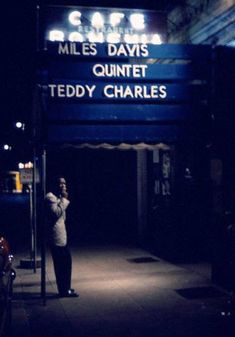 a woman standing in front of a theater sign at night with her phone up to her ear