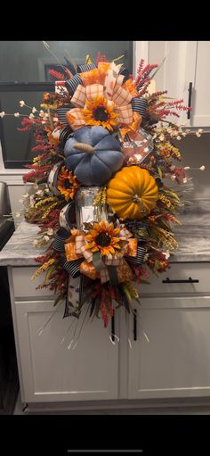 an arrangement of fall flowers and pumpkins on a kitchen counter