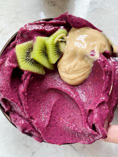 a person is holding up a purple smoothie with kiwi slices and peanut butter on top