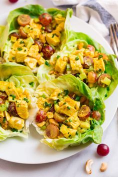 lettuce wraps filled with chicken and vegetables on a white plate next to cranberries