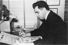 a man sitting at a desk in an office writing on a piece of paper while holding a pen