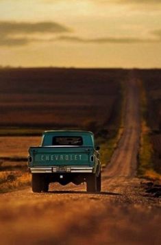 an old pick up truck parked on the side of a dirt road in front of a field