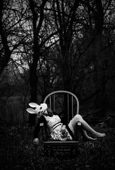 a black and white photo of a woman laying on a bed in the grass with trees behind her